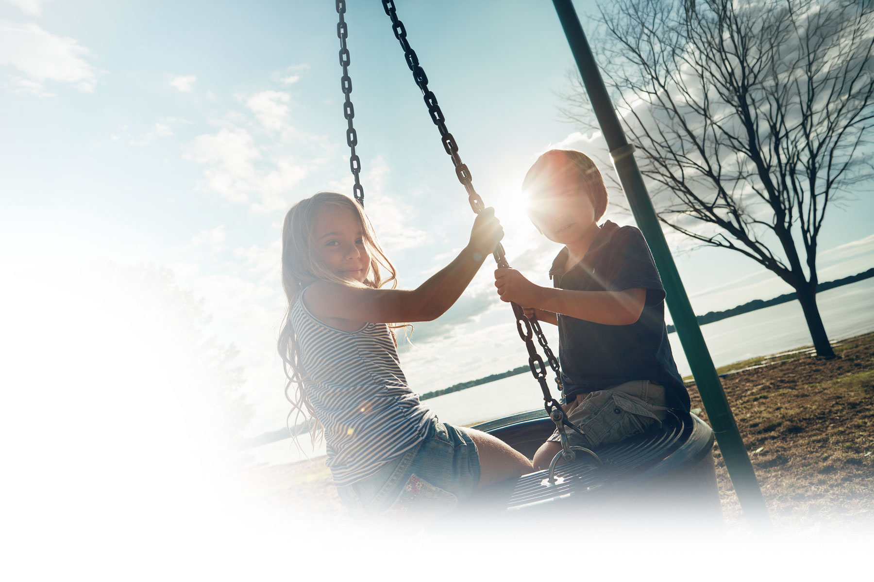 young boy and girl happily playing and swinging on a tire swing