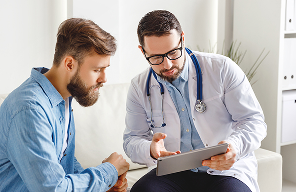 Physician talking with male patient, both looking at touchscreen pc